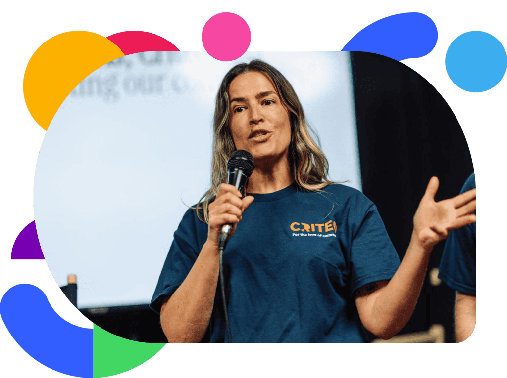 Woman wearing a Criteo T-shirt speaking into a microphone during a company event, gesturing while presenting on stage.