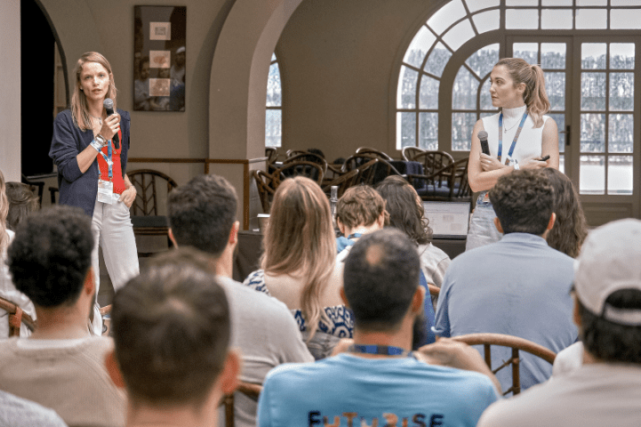 Two women holding microphones presenting to a seated audience during a Criteo workshop or team event in a bright conference space.