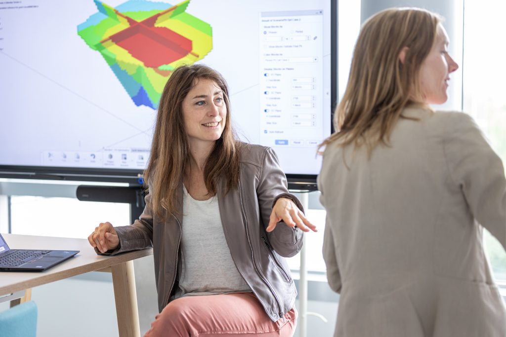 Two colleagues discussing a project in front of a screen displaying a colorful 3D simulation model in a Dassault Systèmes workspace.