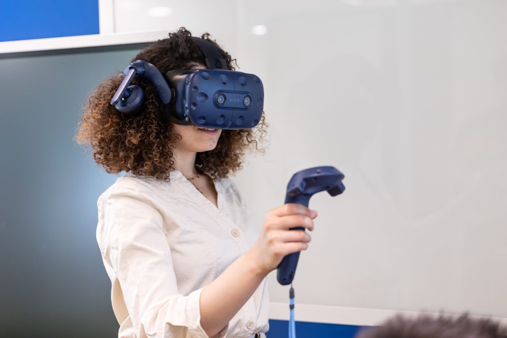 Woman using a VR headset and controller to interact with a virtual environment during a technology demonstration.